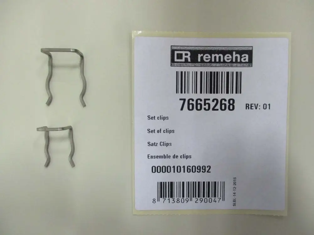 Set aus zwei Metallclips von Remeha, zusammen mit einem Etikett, das Artikelnummer und Bezeichnung enthält. Clips sind auf einem hellen Untergrund angeordnet.